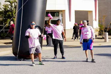 Three diverse people wearing pink in support of those with breast cancer posing for photo in an outdoor setting