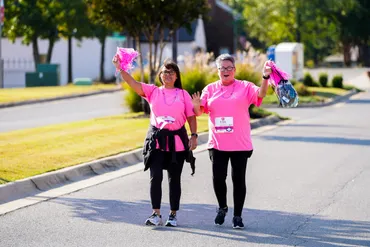 Two women wearing pink walking together in support of those with cancer